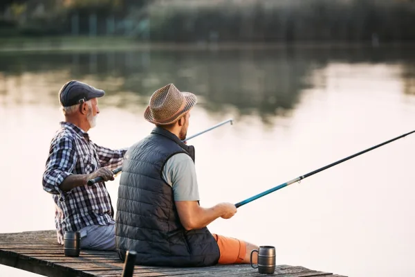 Two anglers fishing together from a wooden jetty on a still lake
