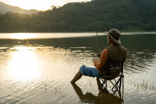An angler seated at the water’s edge at sunrise, rod out over a calm lake