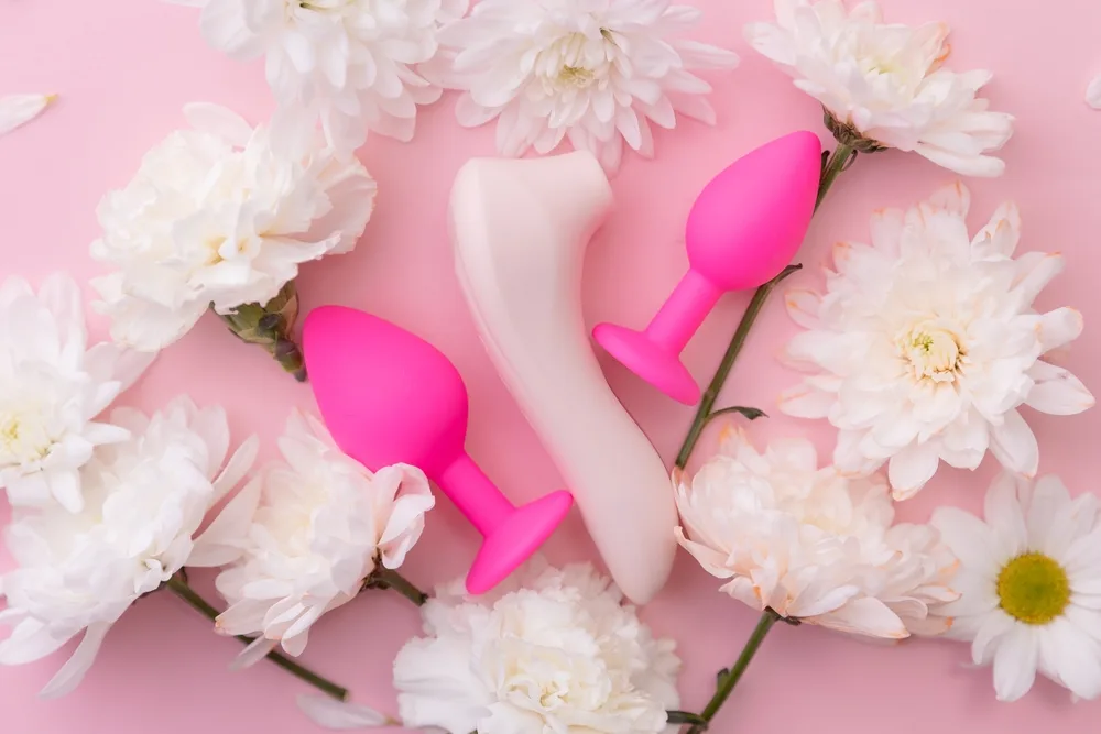 Adult wellness products styled with white flowers on a pink background