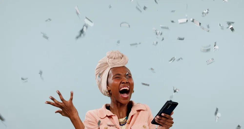 A woman celebrating with her phone as confetti falls around her
